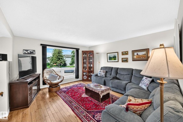 Living room with a grey sectional sofa, red oriental rug, coffee table, and a large window with outdoor view. - 371 Kirkpatrick Cr Nw, Edmonton