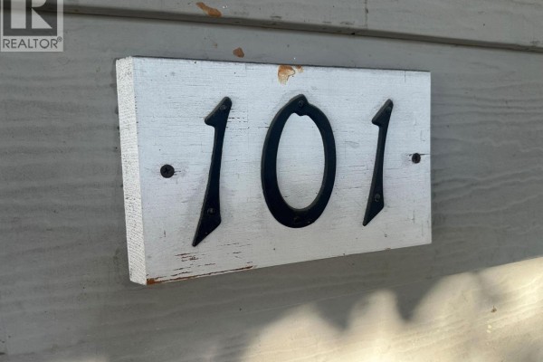 Close-up of the unit number "101" mounted on a distressed white wooden plaque on grey siding. - 3710 24 Avenue Unit# 101, Vernon