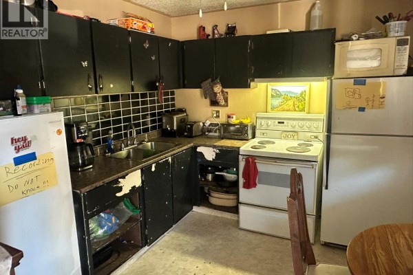 U-shaped kitchen with black cabinets, stainless steel sink, white stove, white refrigerator, and a tiled backsplash. - 3710 24 Avenue Unit# 101, Vernon