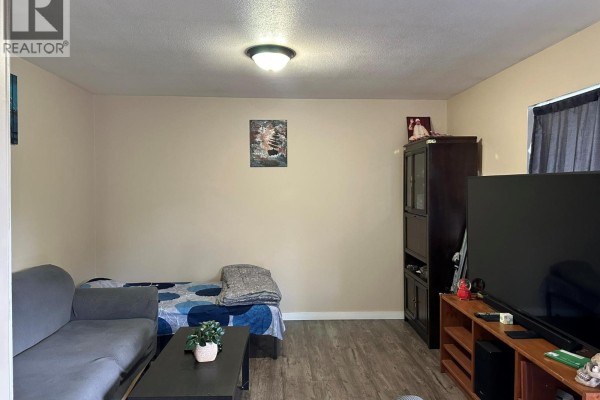 Living room with grey sectional sofa, bed, television, and dark wood cabinet. - 3710 24 Avenue Unit# 202, Vernon