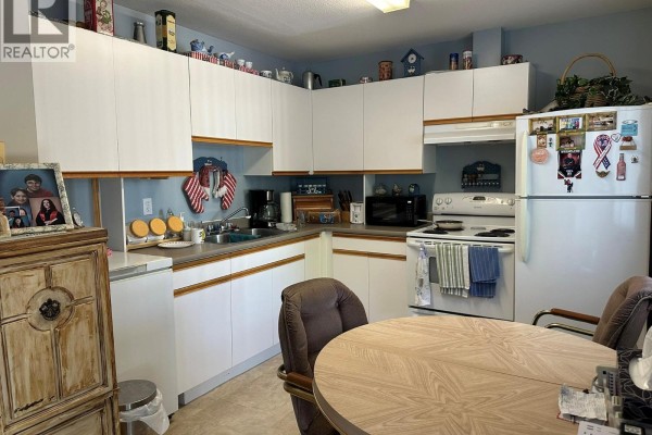 A corner kitchen with white cabinets, beige countertops, and white appliances. - 3712 24 Avenue Unit# 105, Vernon