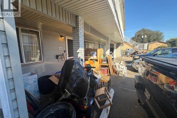 Exterior view of unit 106 entrance and cluttered walkway with vehicles parked nearby. - 3712 24 Avenue Unit# 106, Vernon