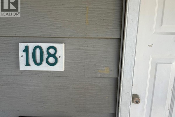 Close-up of the unit number 108 sign mounted on the grey exterior siding. - 3712 24 Avenue Unit# 108, Vernon