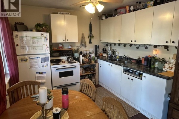 A kitchen with white cabinets, stove, refrigerator, and a wooden dining table. - 3712 24 Avenue Unit# 108, Vernon