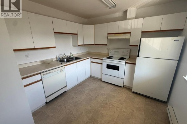 White L-shaped kitchen with white appliances and wooden accents. - 3712 24 Avenue Unit# 205, Vernon