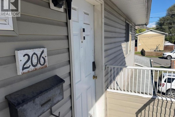 Exterior view of a white door and windows with grey siding, number 206 sign, and a white railing. - 3712 24 Avenue Unit# 206, Vernon