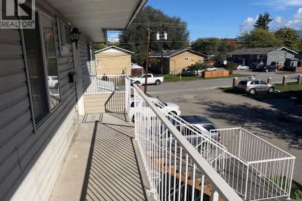 View of a street and houses from a balcony with white railings. Cars are parked below. - 3712 24 Avenue Unit# 206, Vernon
