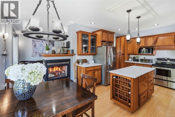 Kitchen and dining area with a gas fireplace, stainless steel appliances, and wood cabinetry. - 3712 Cavendish Blvd, Nanaimo