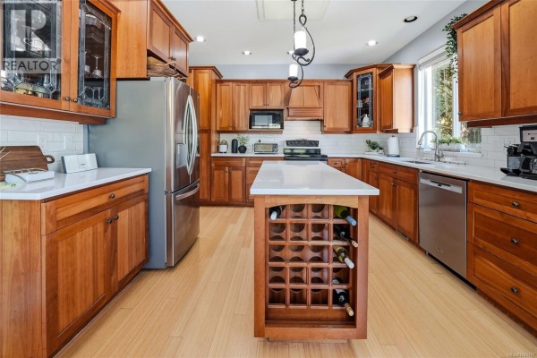 View of the spacious kitchen with light wood cabinets, a white island, and stainless steel appliances. - 3712 Cavendish Blvd, Nanaimo