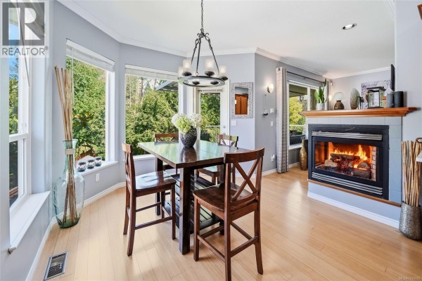 Dining area with large windows, a dark wood table, and a fireplace with a wood mantle. - 3712 Cavendish Blvd, Nanaimo