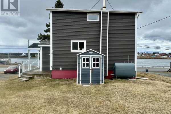 Rear view of house showing dark gray siding, a small gray shed, and a large fuel tank. - 3712 Highway 206, Haut De La Baie