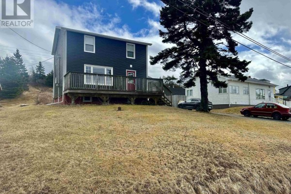 View of house from across a grassy yard, with a deck, a tree, and neighboring houses. - 3712 Highway 206, Haut De La Baie
