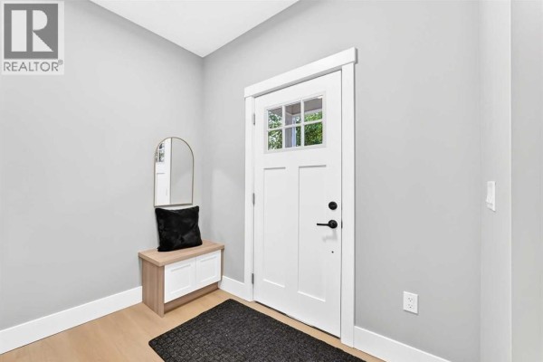 Entryway with a white front door with glass panes, light gray walls, and a wood and white bench. - 3715 14a Street Sw, Calgary