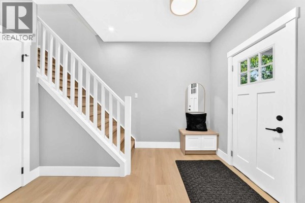 Entryway with a white front door, stairs, and light wood flooring. - 3715 14a Street Sw, Calgary
