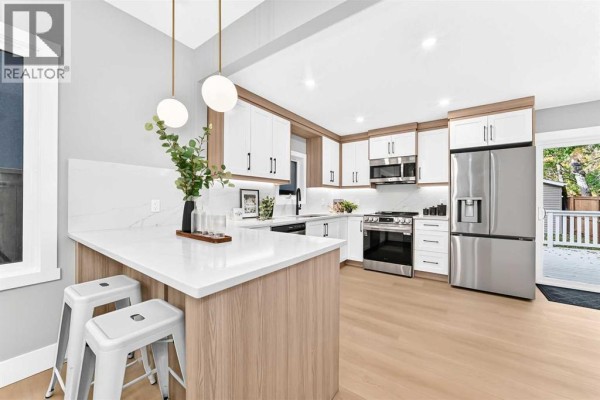 Modern kitchen with white and wood cabinets, stainless steel appliances, and an island with bar stools. - 3715 14a Street Sw, Calgary