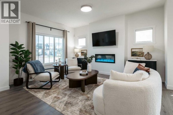 Living room with beige sofa, chairs, coffee table, fireplace, and large window. - 372 Belmont Park Sw, Calgary