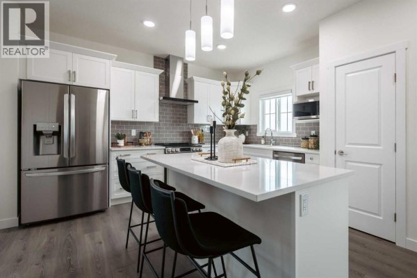Modern kitchen with white cabinets, stainless steel appliances, grey tile backsplash, and island. - 372 Belmont Park Sw, Calgary