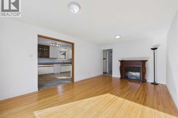 Living room with hardwood floors, white walls, a dark wood fireplace surround, and view into kitchen. - 3720 44 Street, Red Deer
