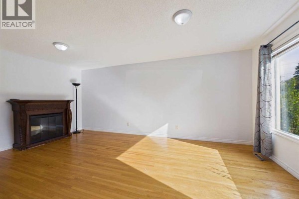 Living room with hardwood floors, white walls, fireplace, floor lamp, and large window with curtains. - 3720 44 Street, Red Deer