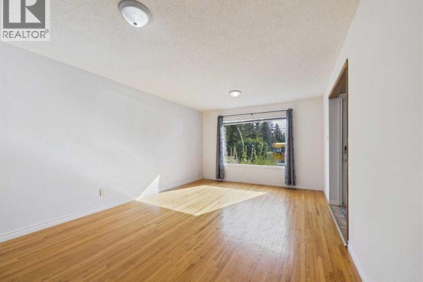 Living room with hardwood floors, white walls, two ceiling lights, and a large window with green trees outside. - 3720 44 Street, Red Deer