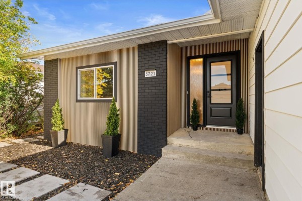 Close-up of the townhouse entrance with a black door, frosted glass panels, and vertical wood accent siding. - 3721 103b Street Nw Nw, Edmonton