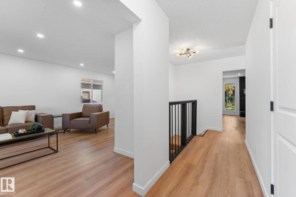 Open-concept living area and hallway featuring white walls, light wood floors, and a black railing. - 3721 103b Street Nw Nw, Edmonton