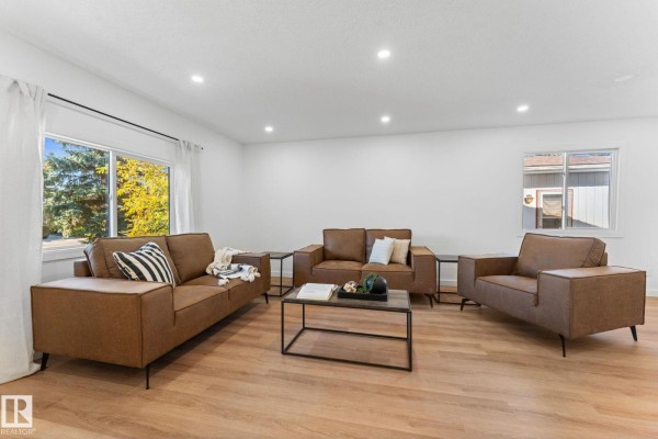 Spacious living room with brown leather sofas, a coffee table, large windows with trees outside, and recessed lighting. - 3721 103b Street Nw Nw, Edmonton