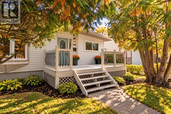 Wider street view of the house with large trees in the foreground and a green lawn leading to the entrance. - 3721 44a Avenue, Red Deer