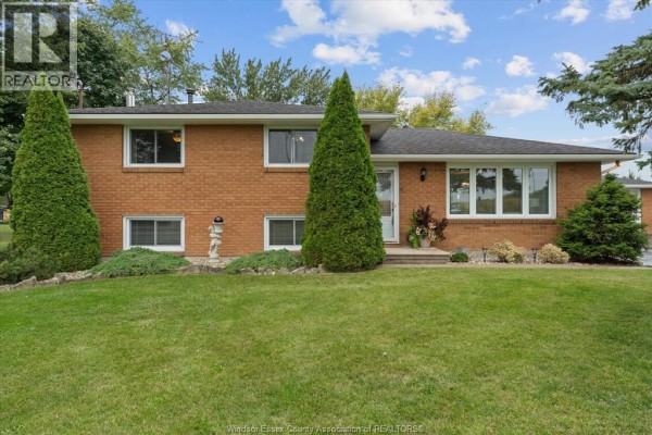 Front view of a red brick house with a manicured lawn and tall evergreen trees. - 3724 Concession 3 Road North, Amherstburg