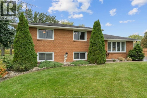 Side exterior view of a brick house with large windows and evergreen landscaping. - 3724 Concession 3 Road North, Amherstburg