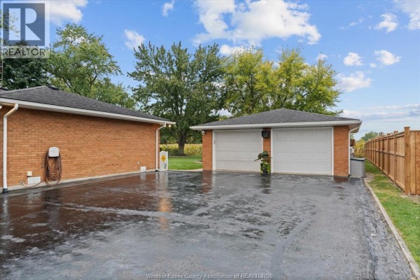Two-car garage with white doors and attached brick building with an EV charger. - 3724 Concession 3 Road North, Amherstburg