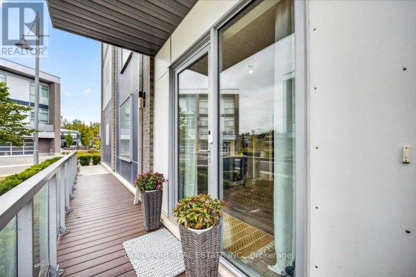 Walkway with wood flooring, glass railing, and potted plants on a townhouse balcony. - 3725 Ferretti Court, Innisfil