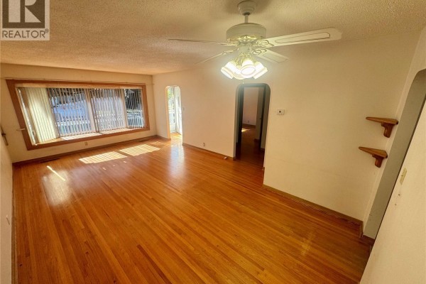 Living room with hardwood floors, large bay window with blinds, and arched doorway. - 3726 Normandy Avenue, Regina