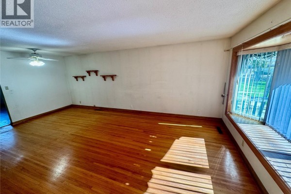 Living room with hardwood floors, white walls, decorative shelves, and large window. - 3726 Normandy Avenue, Regina