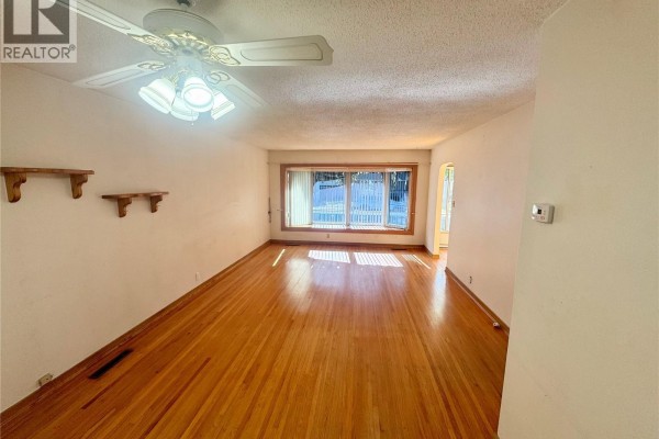 Living room with hardwood floors, white walls, ceiling fan, and large window. - 3726 Normandy Avenue, Regina