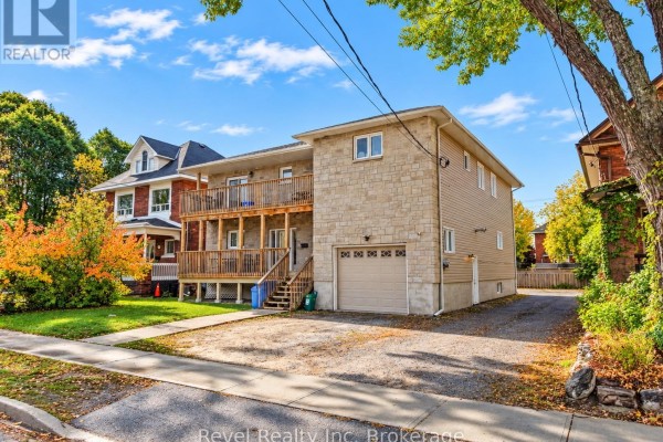 Side view of the multi-family home showing driveway, lawn, and mature trees. - 373 First Avenue E, North Bay