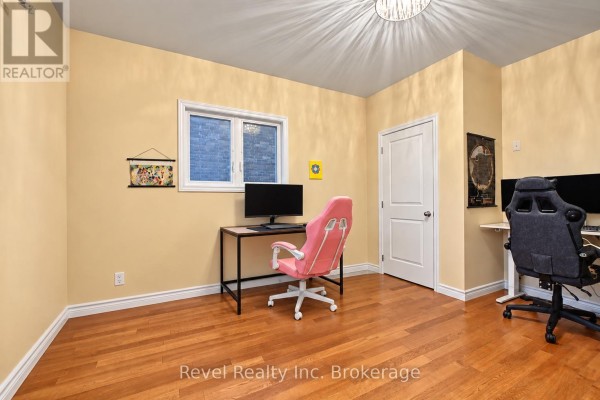 Corner bedroom with light yellow walls, wood floors, and two computer workstations. - 373 First Avenue E, North Bay