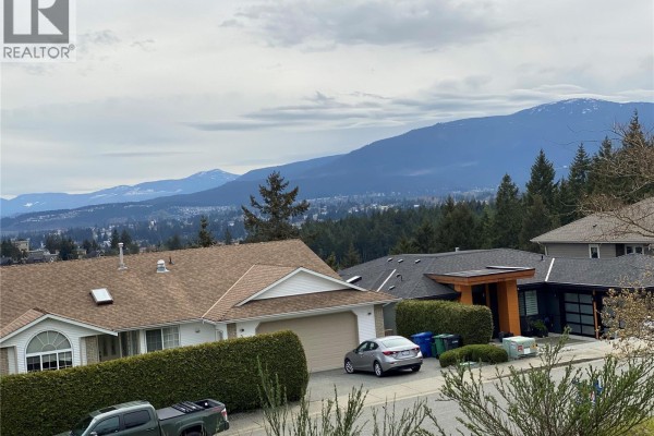 Street view of modern houses with garages, trees, and mountain backdrop. - 3733 Belaire Dr, Nanaimo