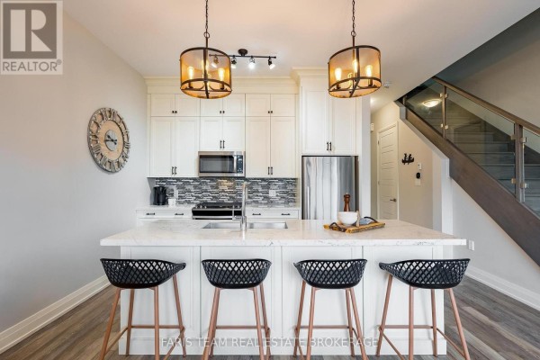 Kitchen island with seating, white cabinetry, and a view of the staircase. - 3733 Riva Avenue, Innisfil