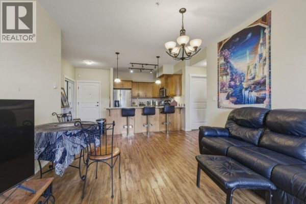 Open living space with kitchen access, dining area, and decorative wall art. - 3739 Casorso Road Unit# 316, Kelowna