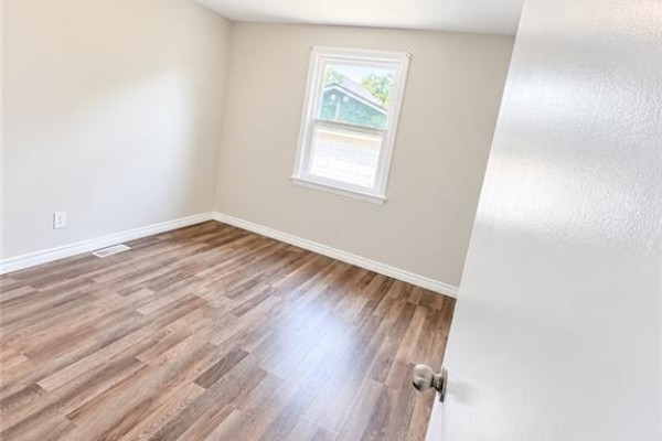 Empty bedroom with light beige walls, a window with a view of trees, and wood-look laminate flooring. - 374 East 15th Street, Hamilton