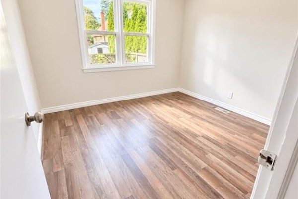 Empty bedroom with light beige walls, a window with a view of trees, and wood-look laminate flooring. - 374 East 15th Street, Hamilton