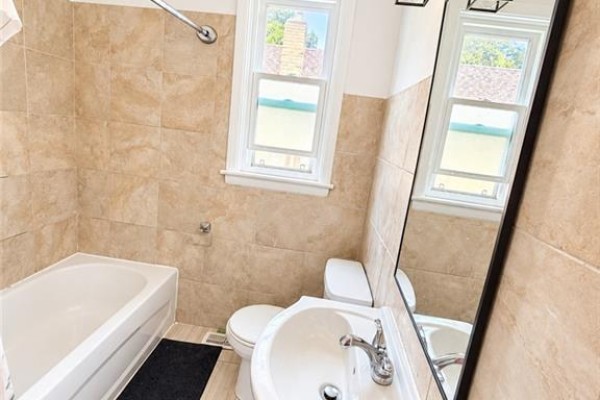 Bathroom with a bathtub, toilet, vanity with sink, beige tiled walls, and a large mirror. - 374 East 15th Street, Hamilton