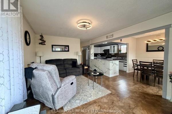 Living room with a sofa, armchair, and view of the kitchen and dining room. - 374 Ste Helene Avenue, Iroquois Falls