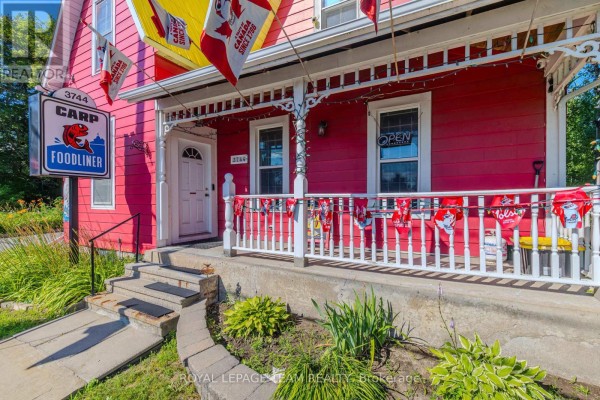 Close-up of a white railing on a red house porch with a 'Carp Foodliner' sign. - 3744 Carp Road, Ottawa