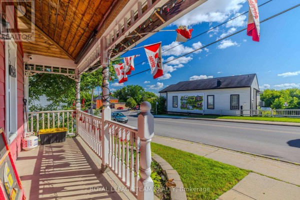 View from a covered porch with white railings, looking across a road at a building. - 3744 Carp Road, Ottawa
