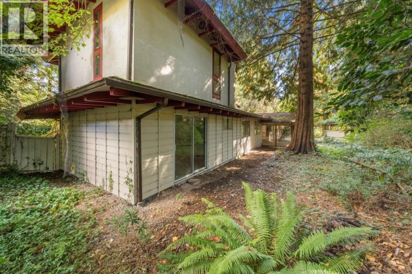 Rear exterior of a multi-story house with beige siding, large windows, and surrounding greenery. - 3745 Southridge Avenue, West Vancouver
