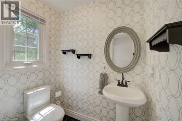 Powder room with white pedestal sink, toilet, patterned wallpaper, and a round mirror. - 375 Holiday Inn Drive Unit# 9, Cambridge