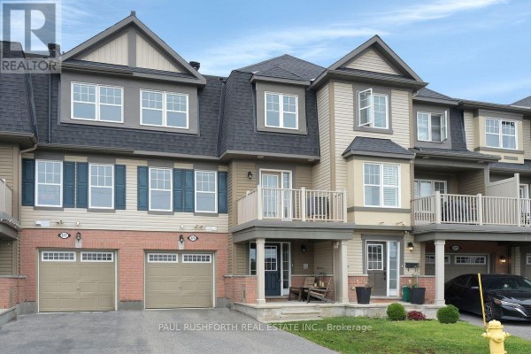 Exterior view of a beige and tan townhouse with dark roof, two garage doors, and balconies. - 375 Sweetfern Crescent, Ottawa