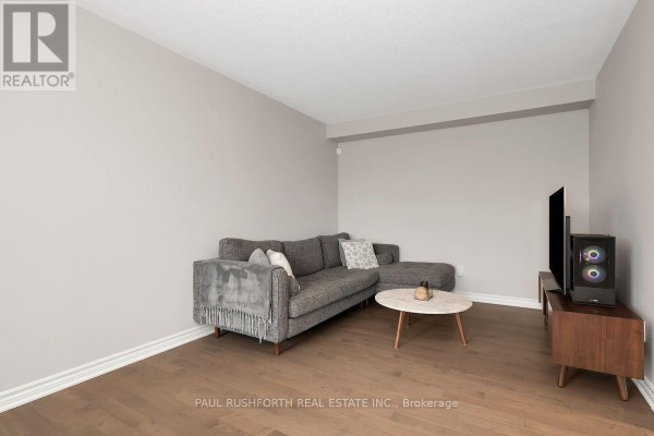 Living room with light grey walls, hardwood floors, a grey sectional sofa, coffee table, and TV console. - 375 Sweetfern Crescent, Ottawa